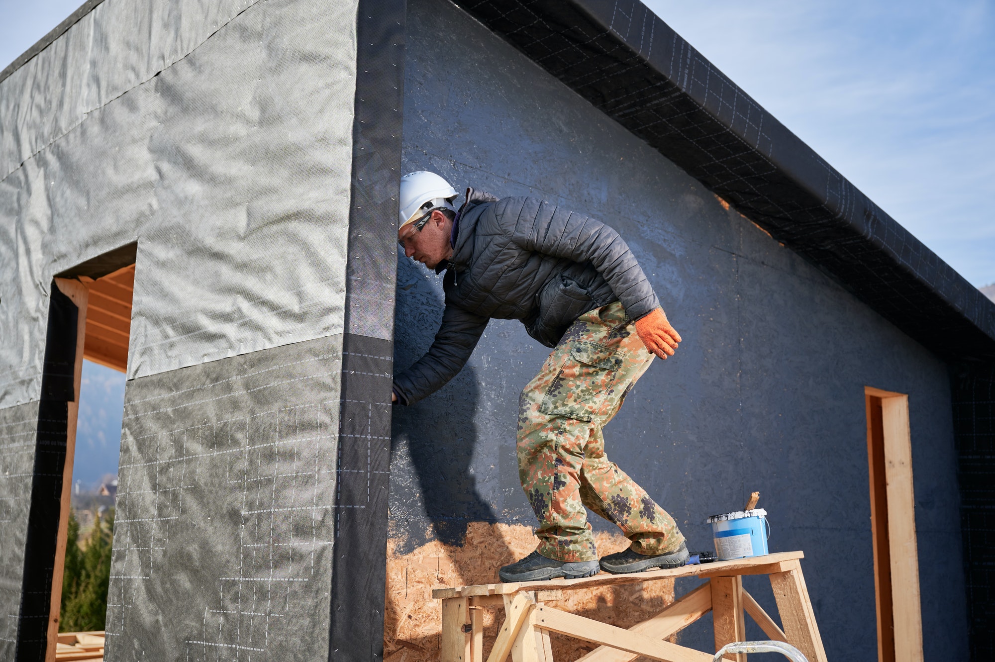 male painter using paint roller doing exterior paint work while building wooden frame house